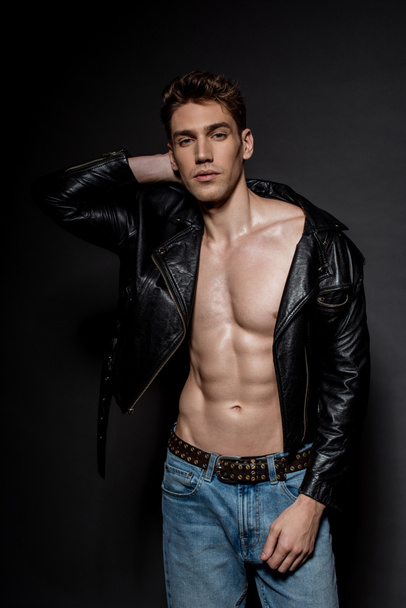 jovem sexy com torso muscular em jaqueta de motociclista e jeans no fundo preto
 - Foto, Imagem