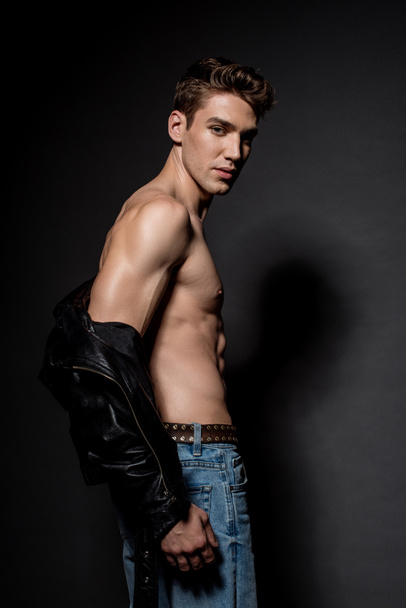 vue latérale de jeune homme sexy avec torse musculaire en veste de motard et jeans sur fond noir
 - Photo, image