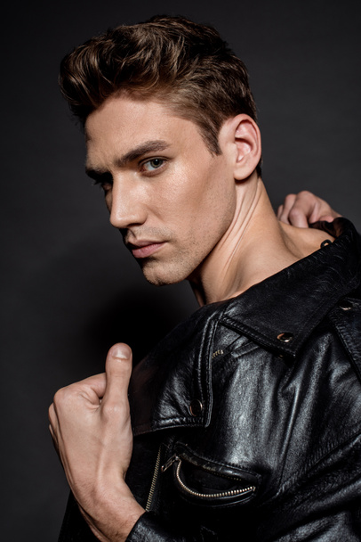 sexy young man with muscular torso in biker jacket looking at camera on black background - Foto, immagini