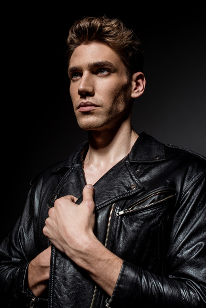 sexy young man in biker jacket looking away on black background - Фото, изображение
