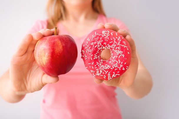 Woman with sweet donut and apple on light background - Foto, Imagen