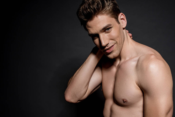 smiling sexy young naked man with muscular torso posing on black background - Photo, Image