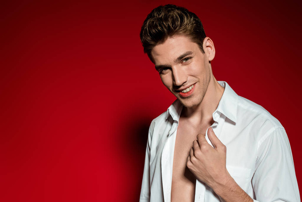 mosolygós szexi fiatal elegáns férfi kigombolt ing piros háttér - Fotó, kép