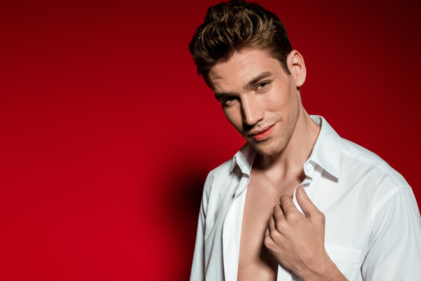 sexy young elegant man in unbuttoned shirt on red background - Zdjęcie, obraz