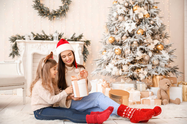 Feliz madre e hija pequeña abriendo regalo de Navidad en casa
 - Foto, Imagen