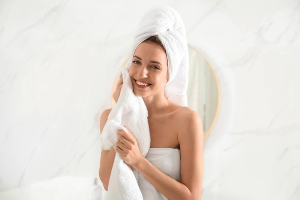 Young woman wiping face with towel in bathroom - Foto, afbeelding