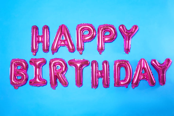 Phrase HAPPY BIRTHDAY made of pink foil balloon letters on light blue background - Fotografie, Obrázek