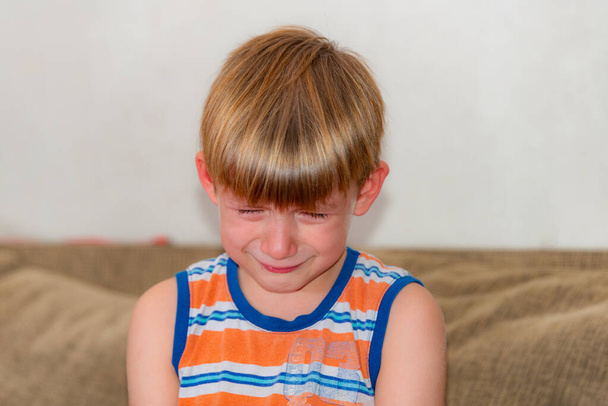 Un niño triste y triste se sienta y llora en el sofá. - Foto, imagen
