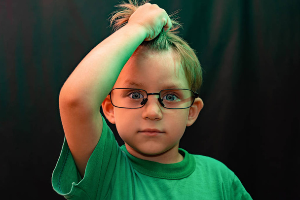 Verrast jongen in bril op een zwarte achtergrond houdt zijn hand met zijn haar en kijkt omhoog - Foto, afbeelding