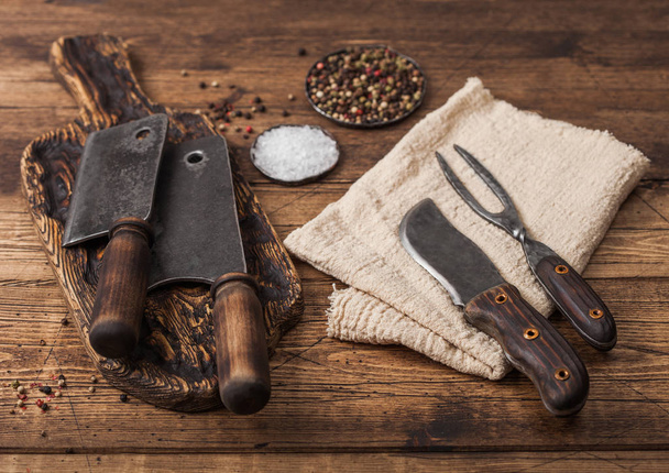Vintage hatchets for meat on wooden chopping board with salt and pepper on wooden table background with linen towel and fork and knife. - 写真・画像