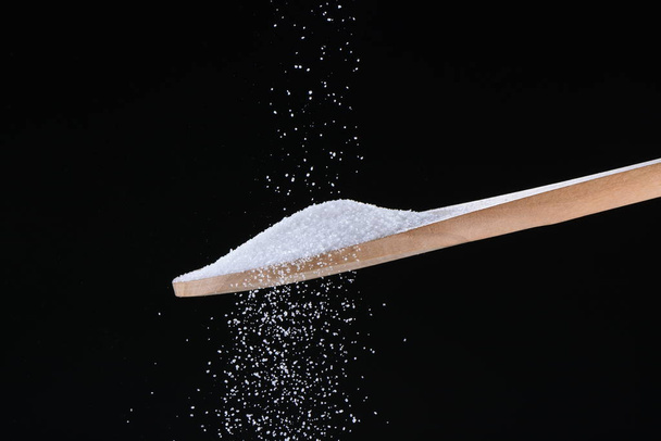 Açúcar caindo em uma colher no fundo preto
 - Foto, Imagem