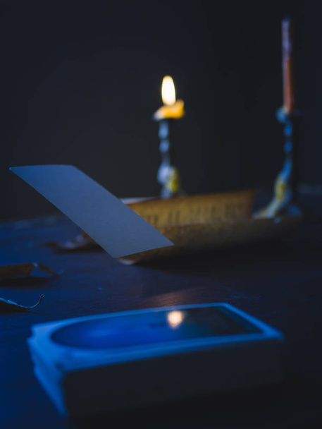 Fotografía de bodegón Low Key, tarjeta flotante del tarot en blanco sobre la mesa en tono oscuro con luz del candelero
 - Foto, imagen