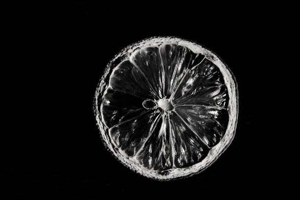 A greyscale shot of a lemon slice on a black background - Photo, image