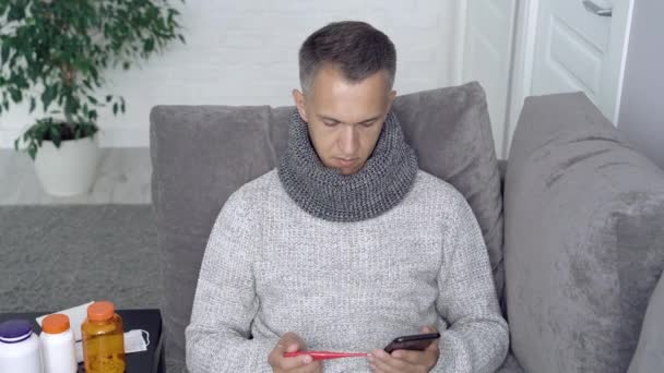 Sick man measuring body temperature and calling the doctor at home - Materiał filmowy, wideo
