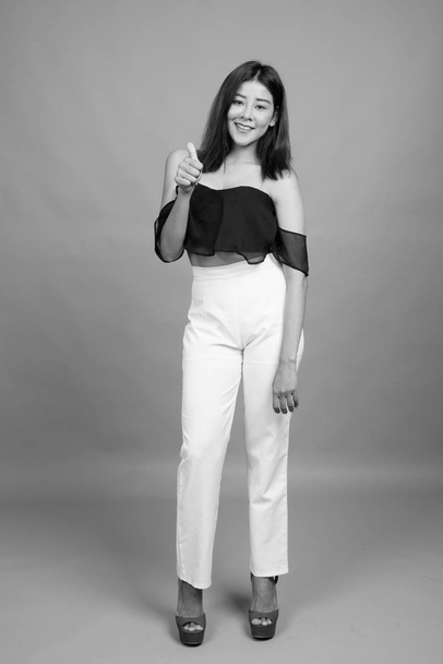 Studio πυροβόλησε νεαρή όμορφη ασιατική γυναίκα γκρι φόντο σε μαύρο και άσπρο - Φωτογραφία, εικόνα