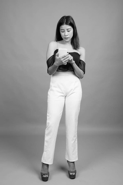 Studio πυροβόλησε νεαρή όμορφη ασιατική γυναίκα γκρι φόντο σε μαύρο και άσπρο - Φωτογραφία, εικόνα