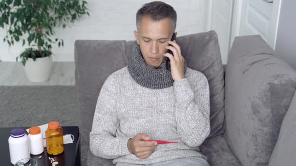 Sick man measuring body temperature and calling the doctor at home - Footage, Video