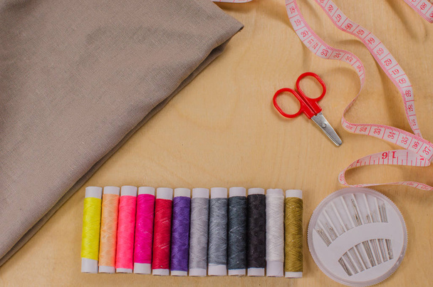 Sewing accessories. Spools of thread with different colors of rainbow, scissors, buttons, measuring tape and accessories for needlework on wooden background. Set for handmade top view - Photo, Image