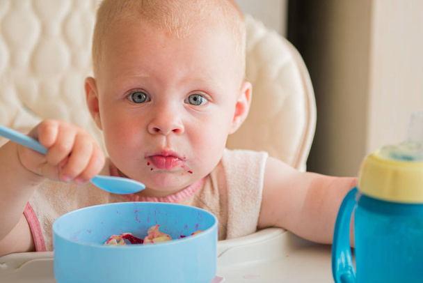 Chłopiec uczy się jeść. słodkie brudne dziecko jedzenie warzyw łyżeczką sam w krzesełku - Zdjęcie, obraz
