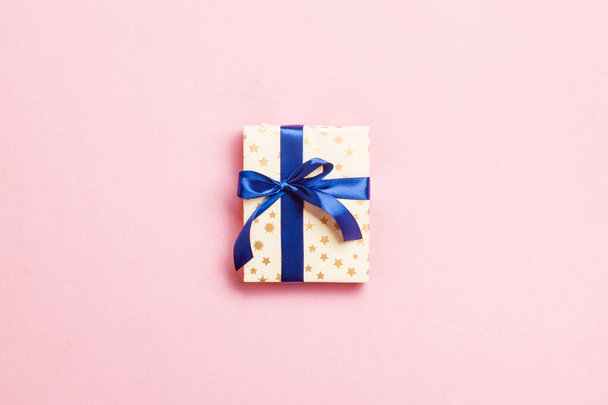 wrapped Christmas or other holiday handmade present in paper with blue ribbon on pink background. Present box, decoration of gift on colored table, top view with copy space - Fotografie, Obrázek
