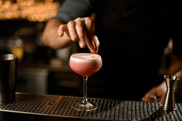 Profesionální barman sloužící růžový alkoholický nápoj zdobený žlutými okvětními lístky - Fotografie, Obrázek