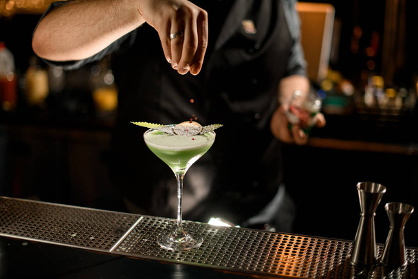 Bartender serving the green creamy color cocktail decorated with a leaf and dried orange sprinkling on it with red pepper peas - Fotografie, Obrázek