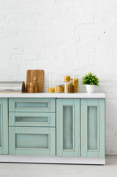 modern white and turquoise kitchen interior with kitchenware, food containers and plant near brick wall - 写真・画像