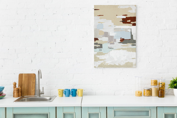 台所用品とレンガの壁に抽象的な絵と近代的な白とターコイズキッチンのインテリア ロイヤリティフリー写真 画像素材