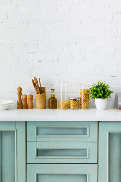 moderne witte en turquoise keuken interieur met keukengerei, voedsel containers en plant in de buurt van bakstenen muur - Foto, afbeelding