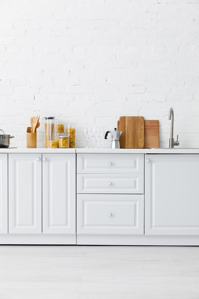 minimalistic modern white kitchen interior with kitchenware near brick wall - Photo, Image