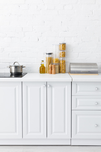 minimalistic modern white kitchen interior with induction cooktop, food, bread box near brick wall - Fotoğraf, Görsel