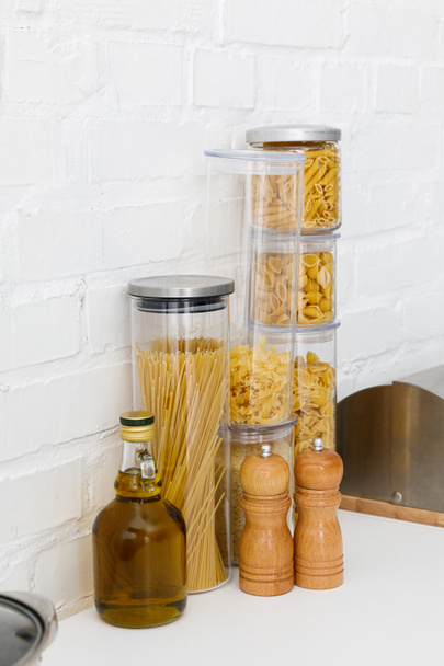 raw pasta in food containers, oil and bread box near white brick wall - Foto, Bild