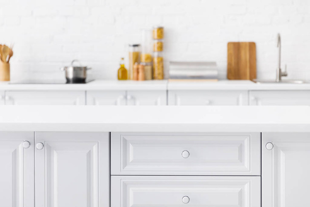 enfoque selectivo de mesa vacía y minimalista moderno interior de cocina blanca con utensilios de cocina y alimentos cerca de la pared de ladrillo en el fondo
 - Foto, Imagen