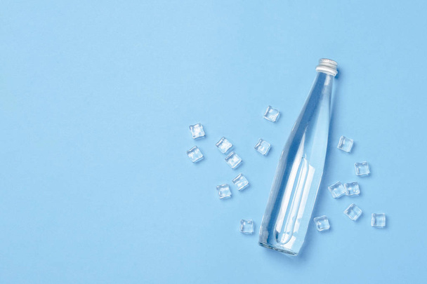 Botella de vidrio con agua clara sobre fondo azul con cubitos de hielo. Concepto de salud y belleza, equilibrio hídrico, sed, calor, verano. Asiento plano, vista superior. Banner - Foto, Imagen