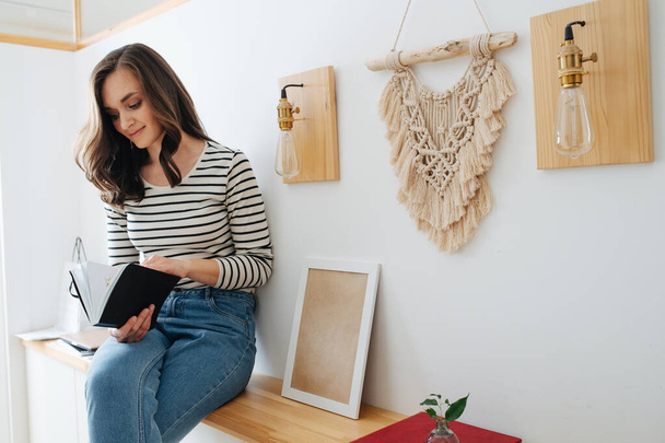 Young happy brunette woman sitting on a shelf, reading book - Photo, Image