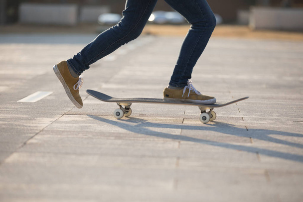Feet of female skateboarder riding board at city park road in sunset - Фото, изображение