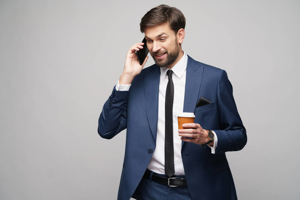 businessman talking on the phone and holding cup of coffee isolated over grey background - Φωτογραφία, εικόνα