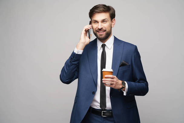 businessman talking on the phone and holding cup of coffee isolated over grey background - Foto, immagini