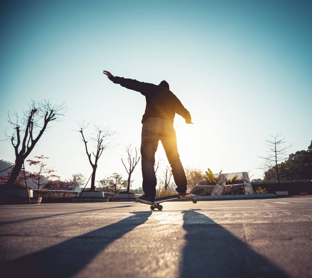 Unrecognizable woman making trick on skateboard at sunset in urban city - Photo, Image