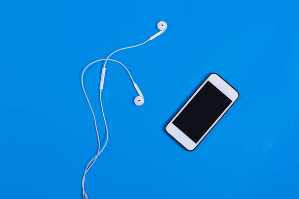 Mobile phone with headphones on a blue background - Photo, Image