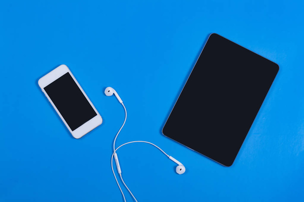 Witte telefoon met zwarte tablet op een blauwe achtergrond - Foto, afbeelding