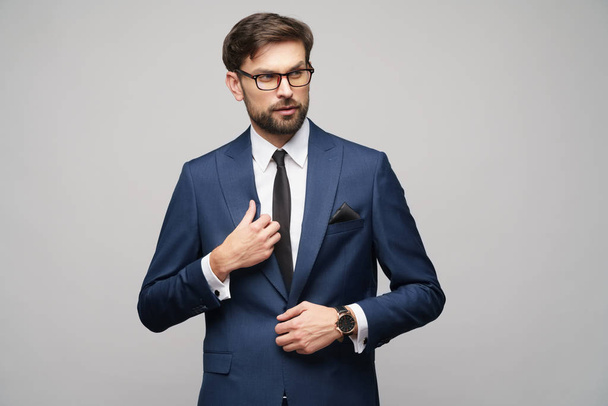 Portrait of a handsome young stylish businessman wearing glasses over grey background - Fotó, kép