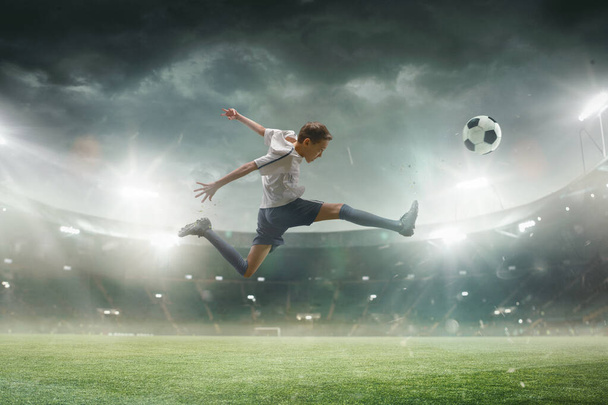 Young male soccer player kicking ball on stadium with flashlights on background - Foto, afbeelding