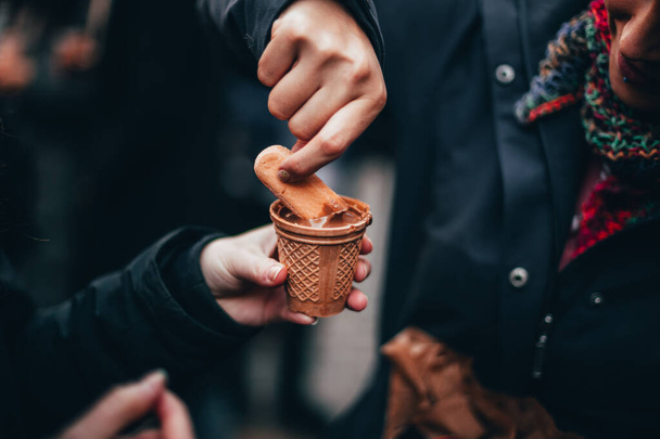 Kobiece ręce jedzące płynną czekoladę na czekoladowym targu w Tuebingen, Niemcy z kabinami świątecznymi i straganami z wieloma ludźmi stojącymi w tłumie pijącymi grzane wino i gorącą czekoladę. - Zdjęcie, obraz