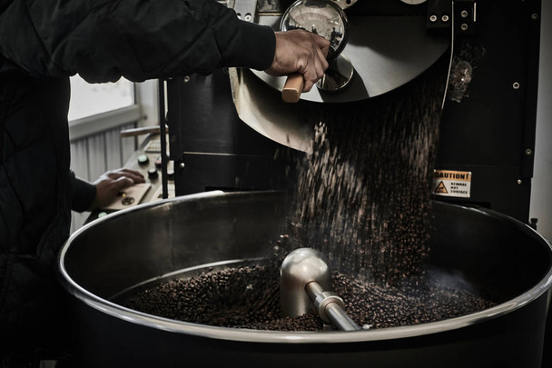 Freshly roasted coffee beans pouring from a large coffee roaster - 写真・画像