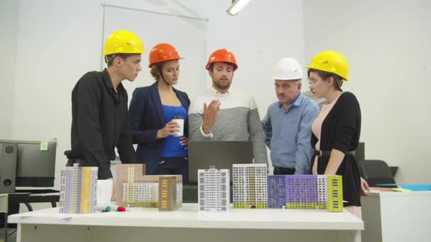 Mensen in helmen bespreken een project en modellen van huizen  - Video