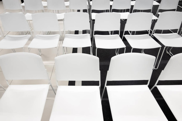 Rzędy białych plastikowych krzeseł na formalne spotkania, konferencje, wykłady, ceremonie ukończenia szkoły. Pokój pełen pustych białych krzeseł. - Zdjęcie, obraz