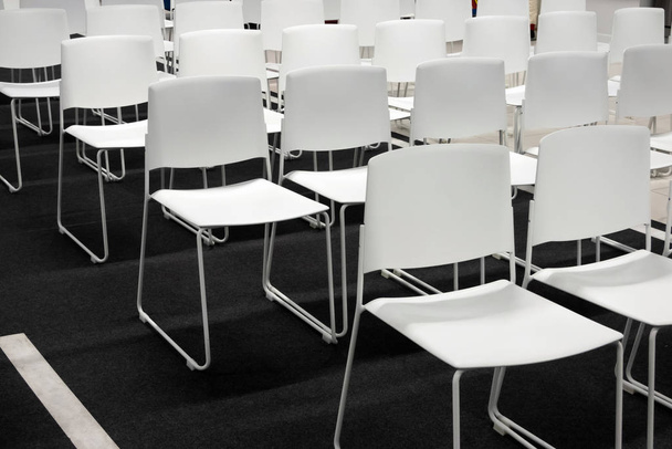 Rzędy białych plastikowych krzeseł na formalne spotkania, konferencje, wykłady, ceremonie ukończenia szkoły. Pokój pełen pustych białych krzeseł. - Zdjęcie, obraz
