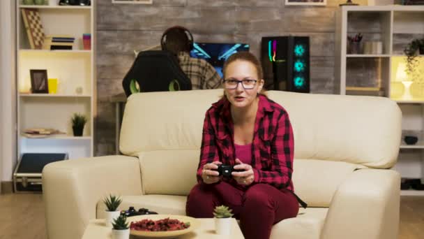 Woman sitting on couch in living room playing video games - Video, Çekim