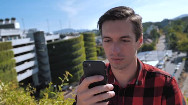 Mladý muž posouvá obrazovku smartphonu. Podnikatel pomocí svého chytrého telefonu a rolování obrazovky venku na střeše ve městě městské pozadí - Záběry, video